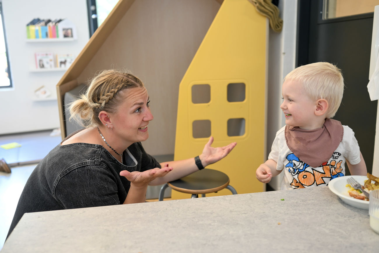 Voksen snakker med barn, der spiser